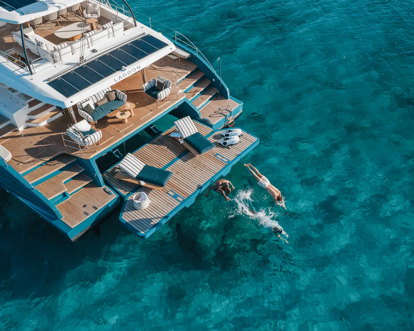 Aerial view of guests swimming off the stern of a luxury catamaran